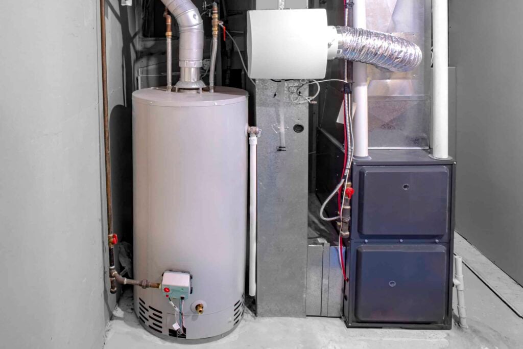 Furnace system with cylindrical water heater, metal air handler unit, and ductwork in basement utility room.