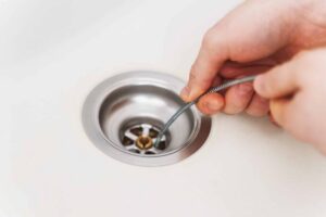 Hand inserting a metal drain snake into a sink drain to clear clogs and blockages.