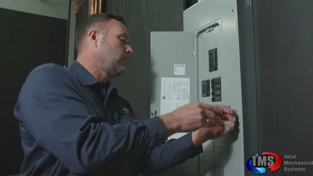 Technician in navy uniform inspecting an electrical panel with circuit breakers and documentation labels on the door.